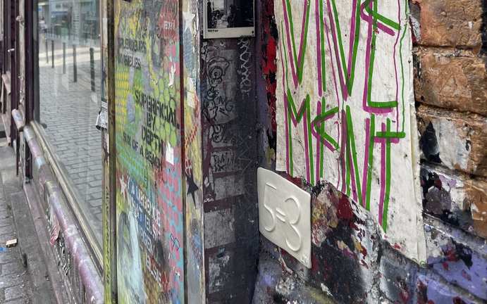 A 5=3 ceramic plaque against a colourful abstract street-art wall
