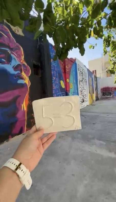A 5=3 ceramic plaque left beside a wall of Rio de Janeiro street art