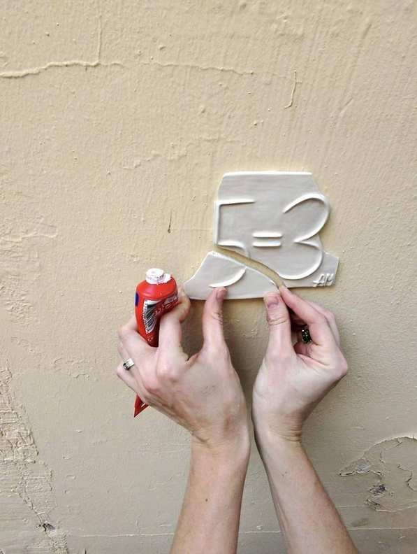 Attaching a ceramic 5=3 plaque to a wall in a graffiti-covered underpass
