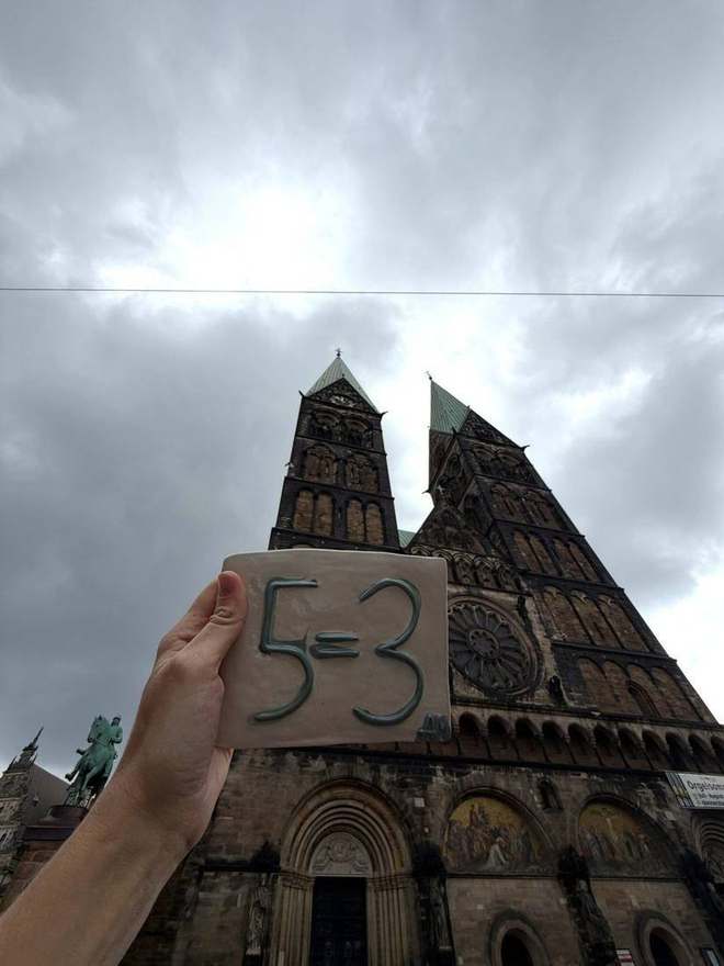 Holding up a 5=3 plaque in front of a cathedral's twin towers