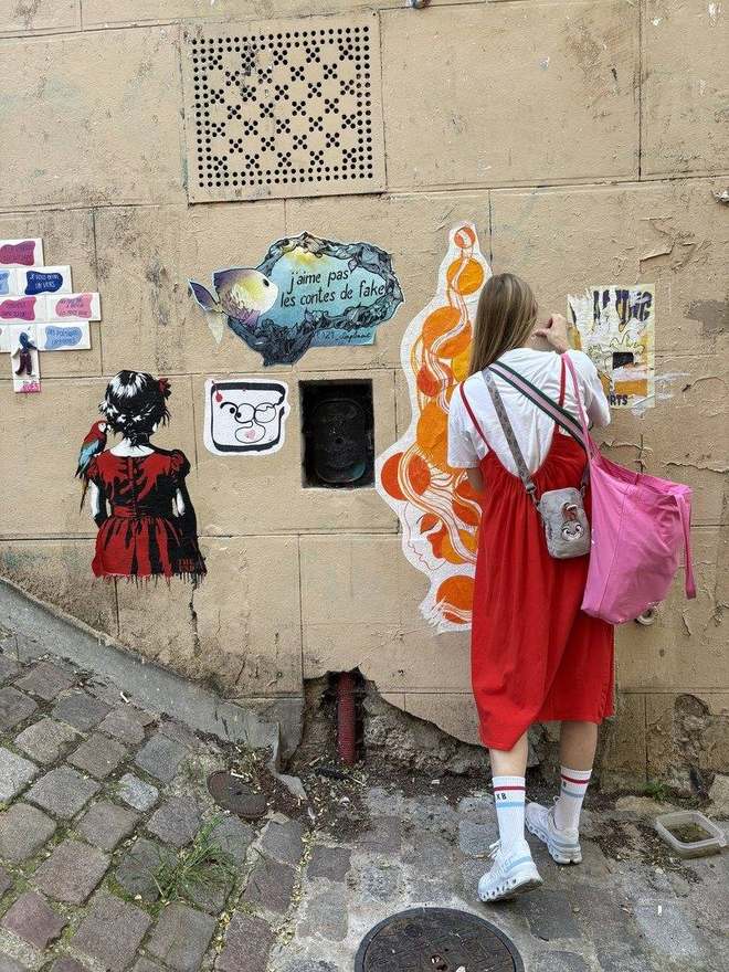 Anna looking at a wall covered in stickers and street art in Paris