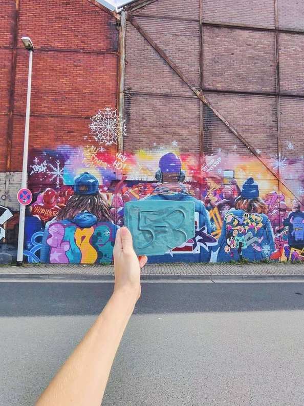 A 5=3 ceramic plaque against a colourful abstract street-art wall