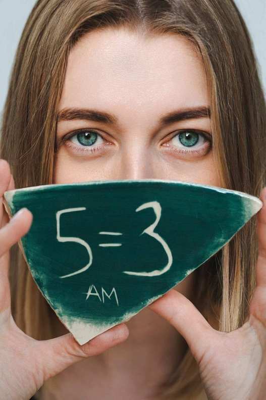 Anna Maslennikov holding a ceramic 5=3 plaque in front of her face